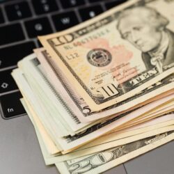Notas de dólar empilhadas sobre um laptop, simbolizando a promessa de dinheiro fácil com IA